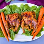 air fryer Cornish hens, fresh spinach, and carrots on a white plate