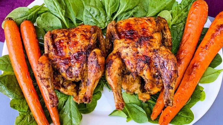 air fryer Cornish hens, fresh spinach, and carrots on a white plate