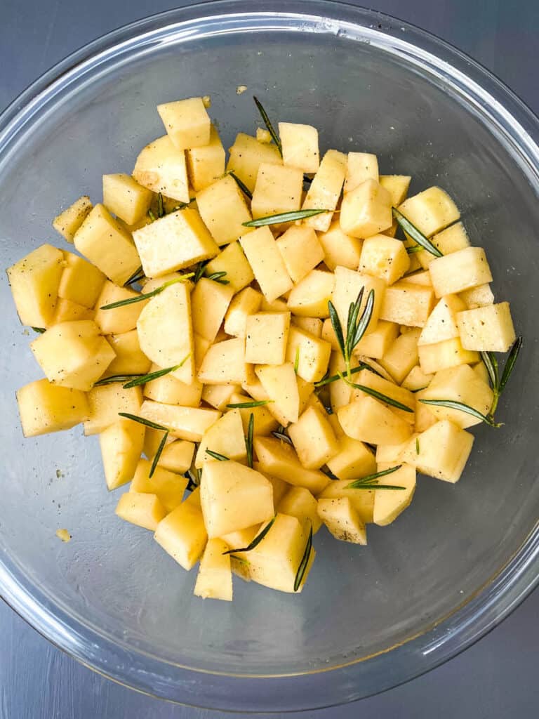 sliced potatoes in a glass bowl with rosemary