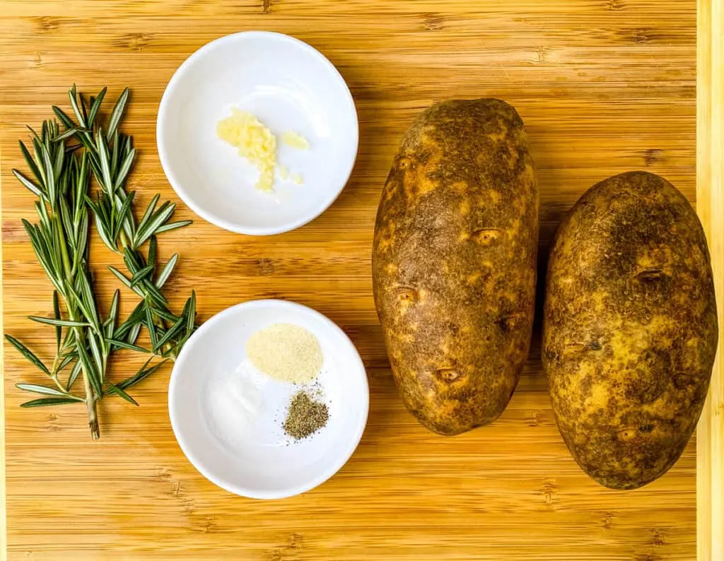 russet potatoes, garlic, and rosemary on a bamboo cutting board