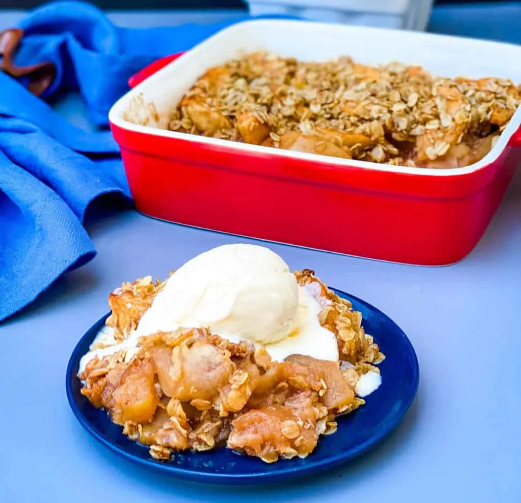 healthy apple crisp on a plate with a scoop of vanilla ice cream with a baking dish of crisp