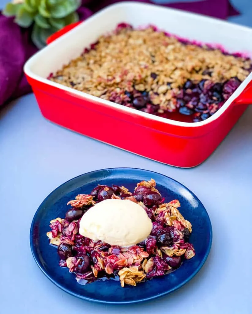 healthy blueberry crisp on a blue plate with a scoop of vanilla ice cream