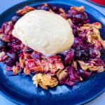 healthy blueberry crisp on a blue plate with a scoop of vanilla ice cream