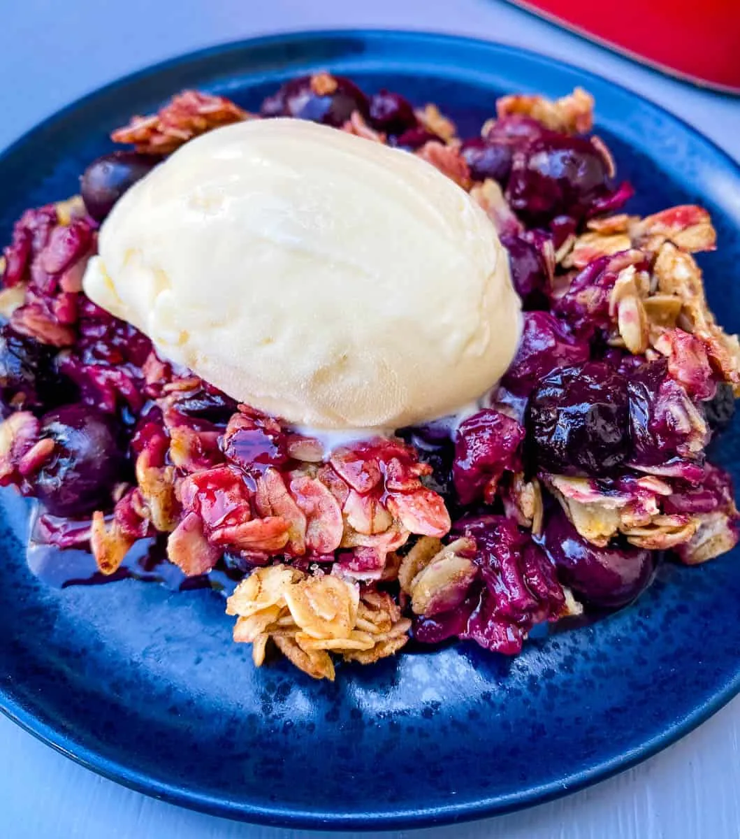 healthy blueberry crisp on a blue plate with a scoop of vanilla ice cream