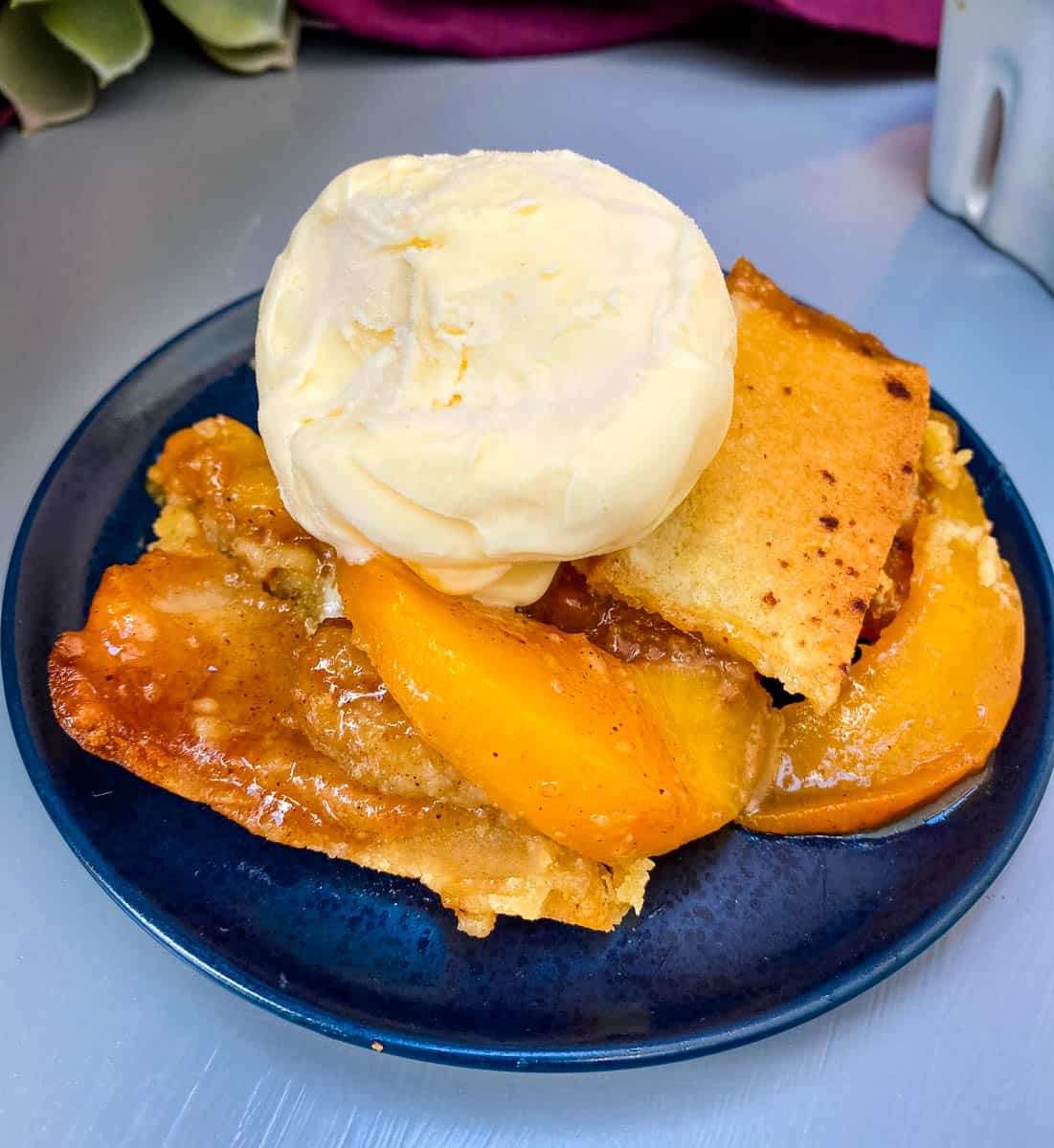 healthy southern peach cobbler on a blue plate with vanilla ice cream