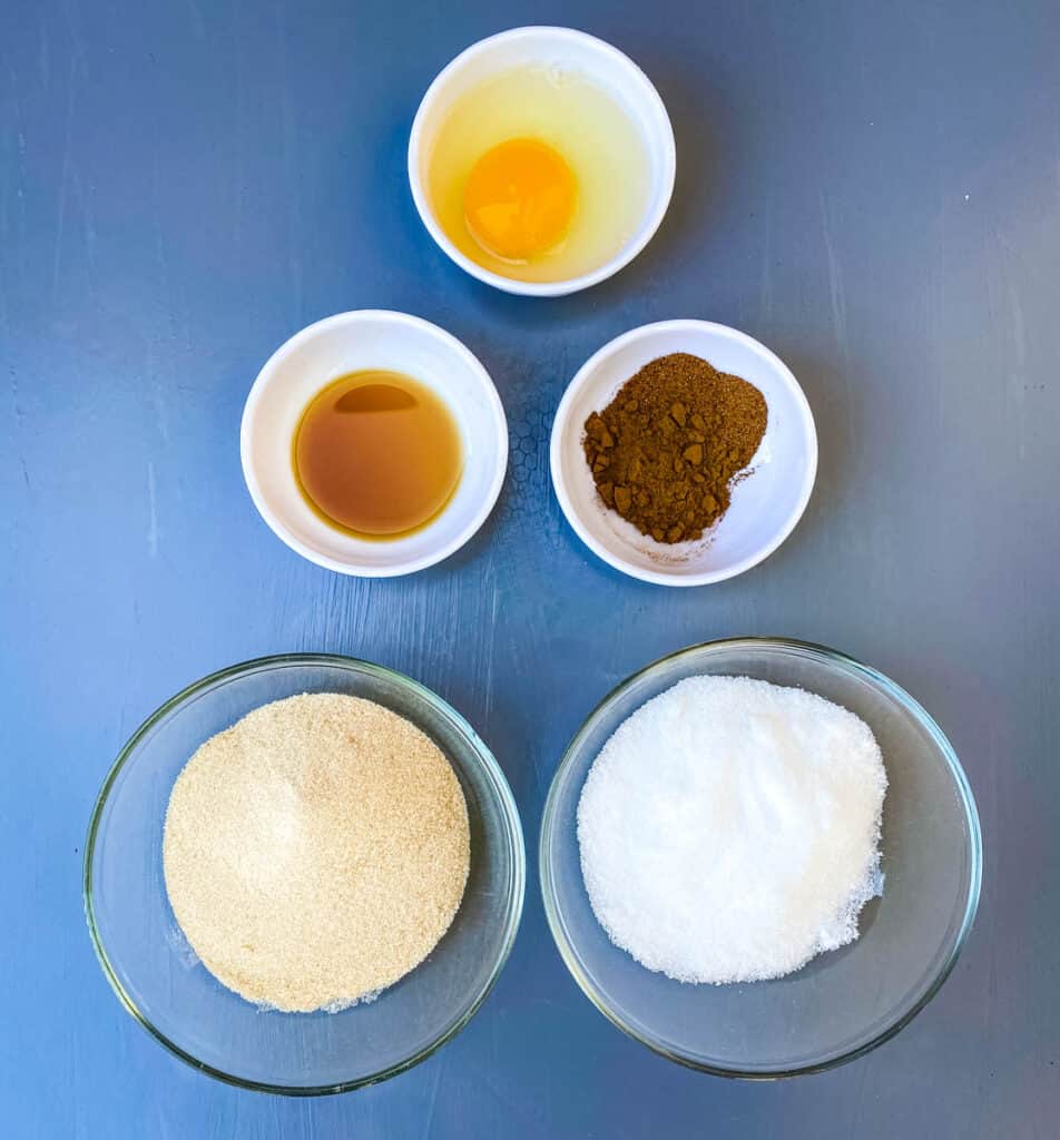 egg, cinnamon, nutmeg, vanilla, brown sweetener, and sweetener in bowls on a flat surface