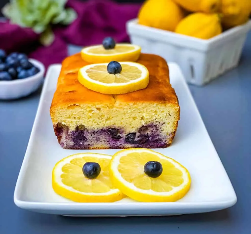 keto low carb lemon blueberry bread on a white plate with fresh lemons and blueberries