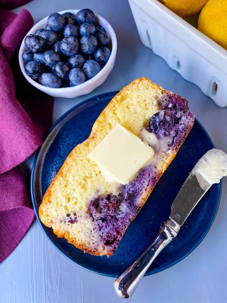 a slice of keto lemon blueberry bread on a blue plate with butter