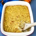 Southern cornbread dressing in a baking dish with a large scoop in a wooden spoon