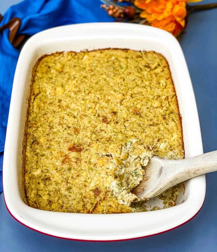 Southern cornbread dressing in a baking dish with a large scoop in a wooden spoon