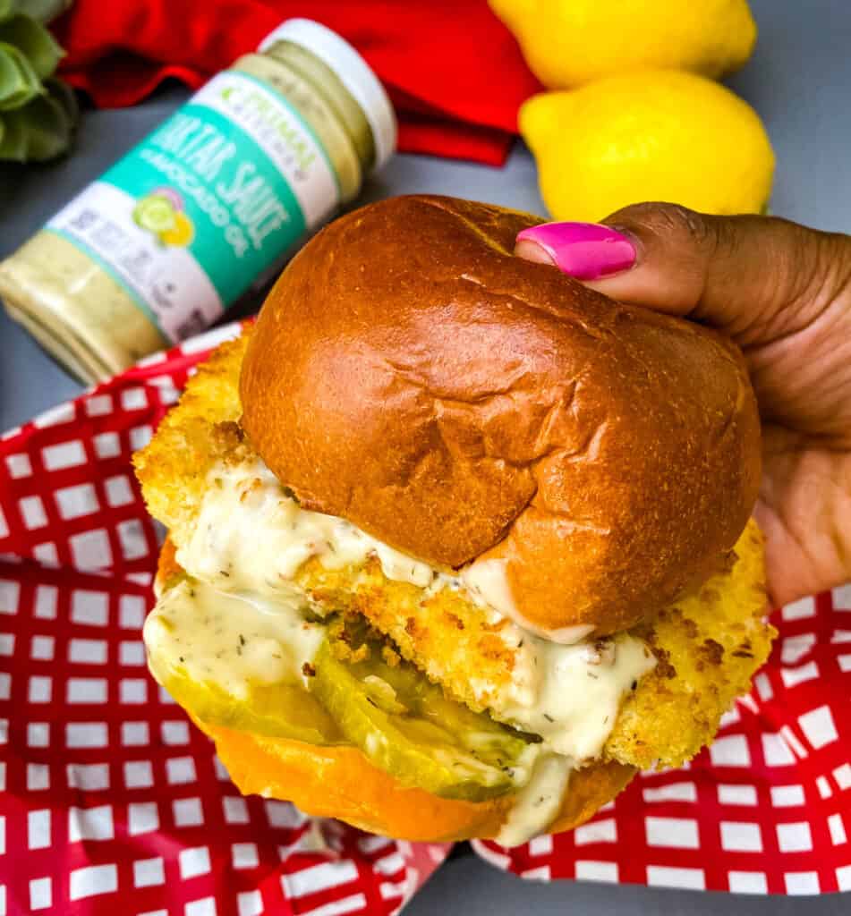person holding air fryer fish sandwich on a bun with melted cheese and tartar sauce