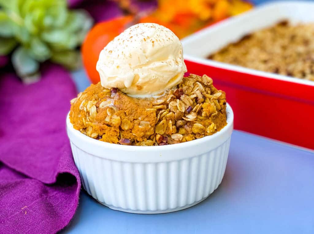 healthy pumpkin crisp in a white bowl with a scoop of vanilla ice cream 