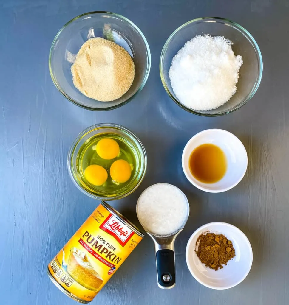 monkfruit sweetener, raw eggs, vanilla, pure pumpkin, pumpkin pie spice, and coconut milk in separate bowls on a flat surface