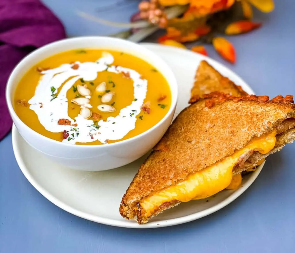 Panera autumn squash soup in a white bowl with a grilled cheese sandwich