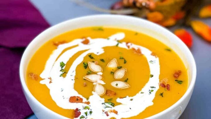 Panera copycat autumn squash soup in a white bowl with seeds and bacon