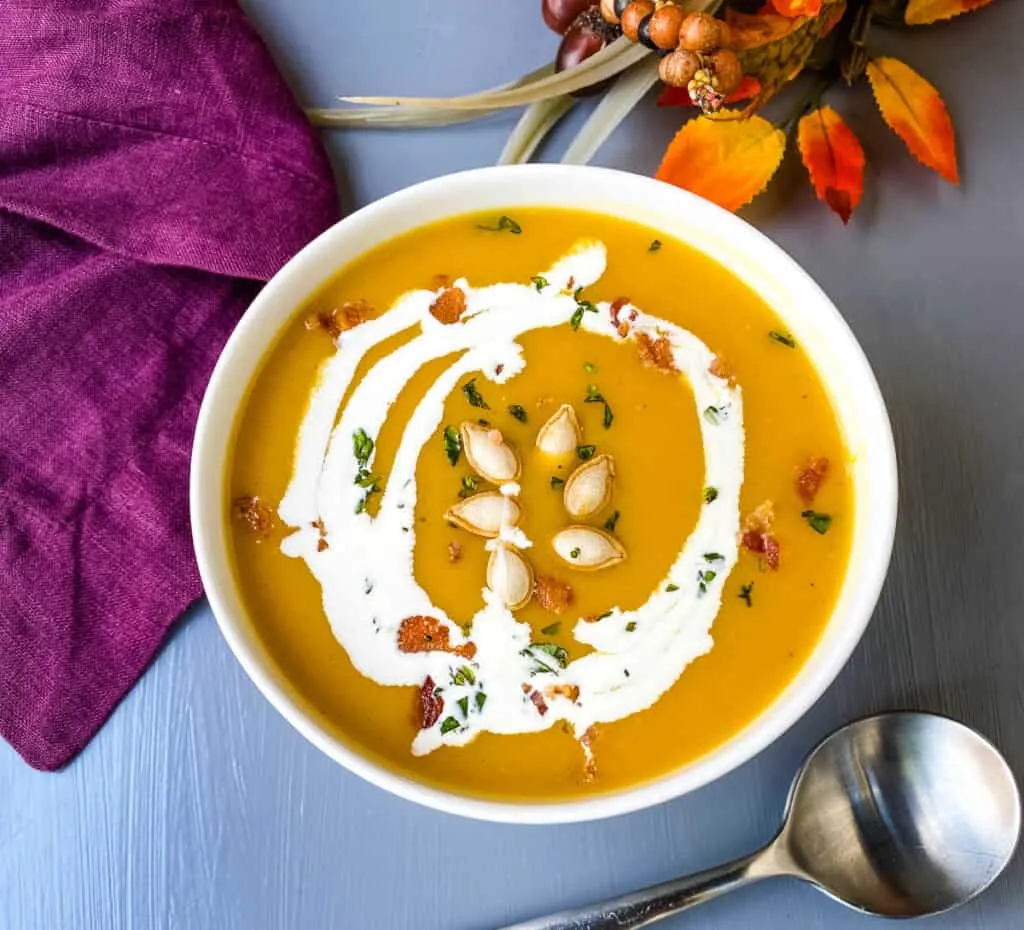 Panera copycat autumn squash soup in a white bowl with seeds and bacon