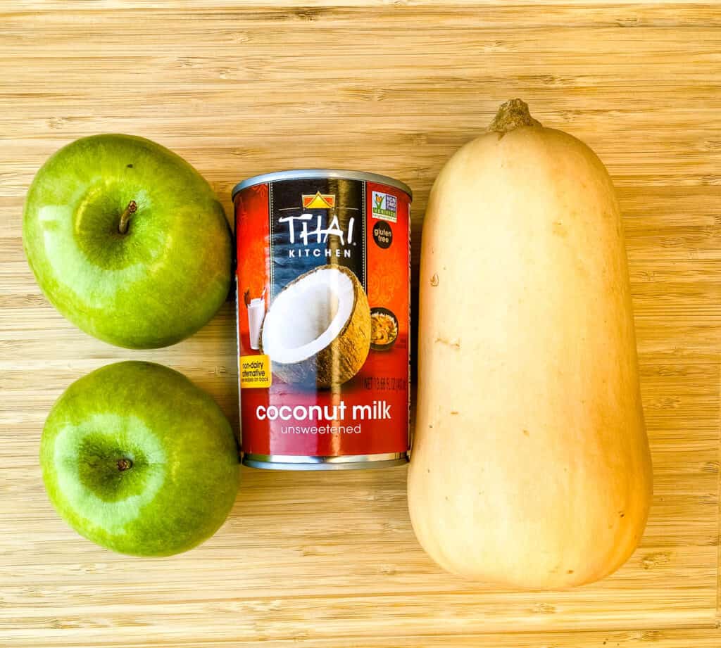 Granny Smith apples, coconut milk, and fresh butternut squash on a wooden cutting board