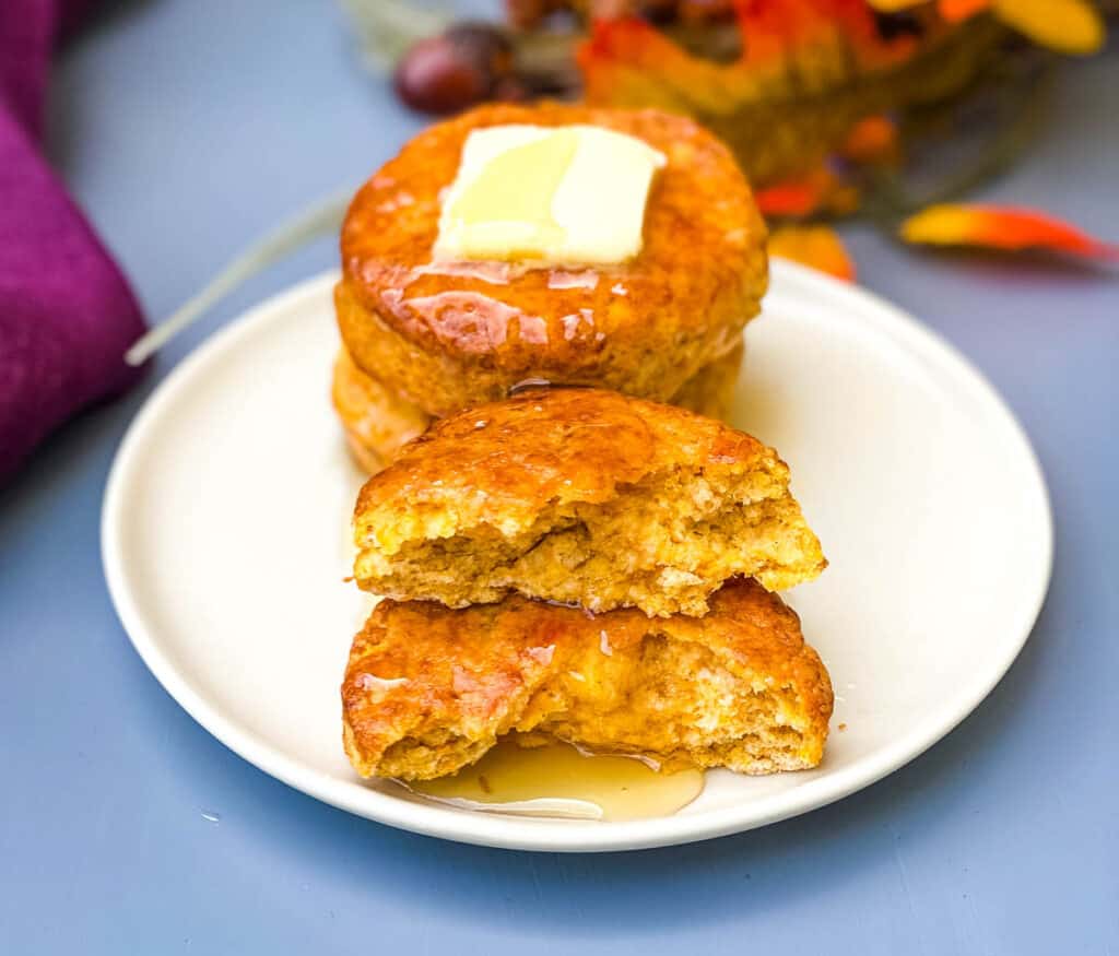 sweet potato biscuits on a white plate with butter, 1 biscuit is cut in half and drizzled with honey