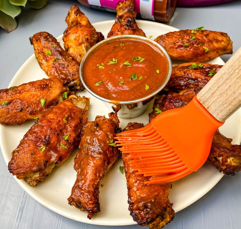 air fryer bbq chicken on a plate with bbq sauce with a cooking brush drizzling sauce over the chicken