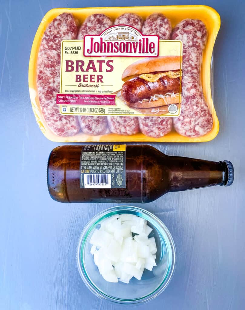 raw uncooked brats, a bottle of beer, and chopped white onions on a flat surface