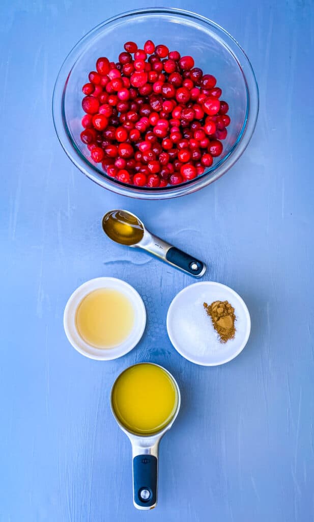 cranberries in a glass bowl alongside orange juice, honey, cinnamon, and sweetener