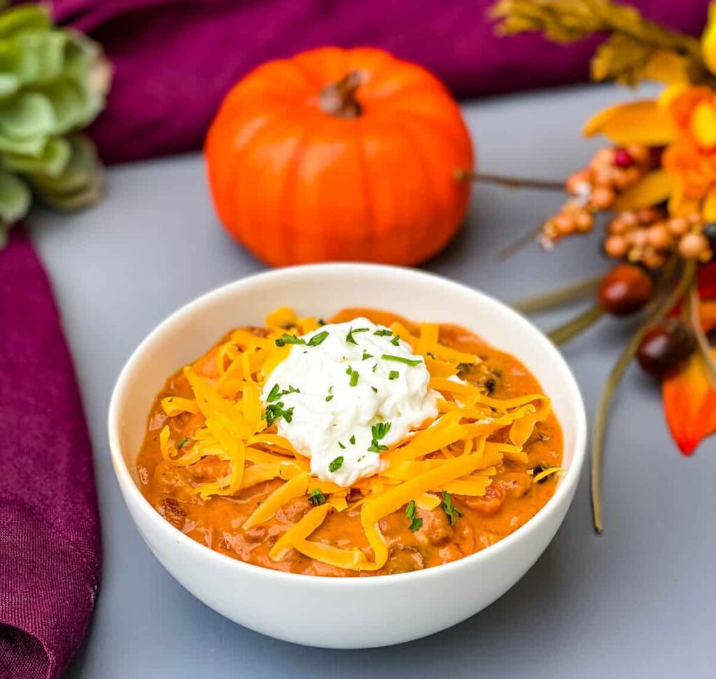 pumpkin chicken chili in a white bowl with a pumpkin and purple napkin in the background