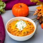 pumpkin chicken chili in a white bowl with a pumpkin and purple napkin in the background