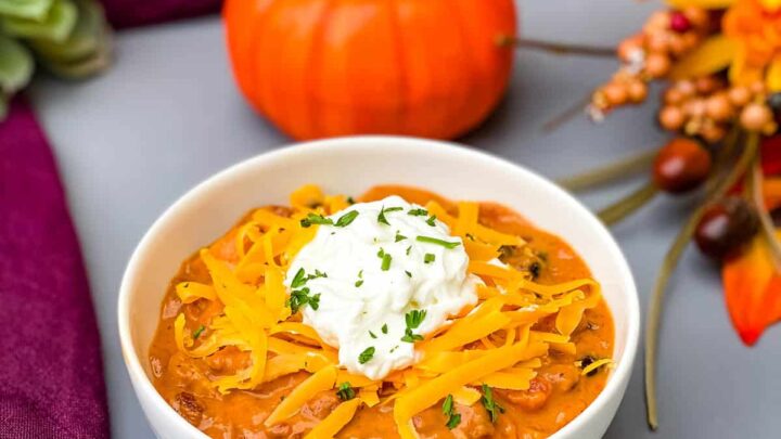 pumpkin chicken chili in a white bowl with a pumpkin and purple napkin in the background