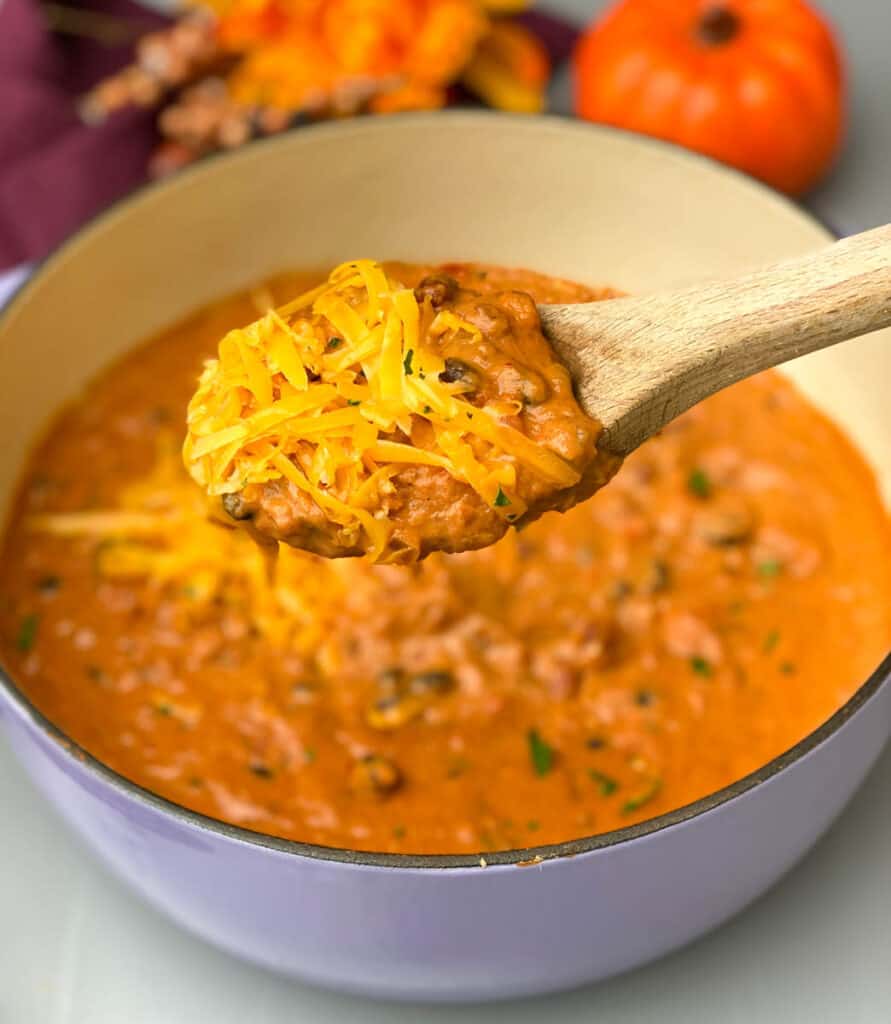 pumpkin chicken chili in a white bowl and chili in a purple Dutch oven with cheese