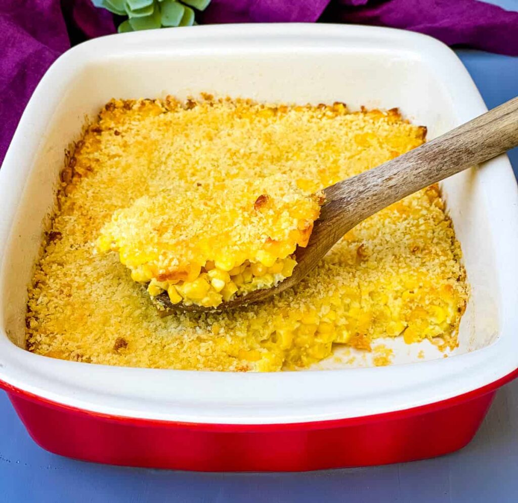 a wooden spoonful of scalloped corn in a baking dish