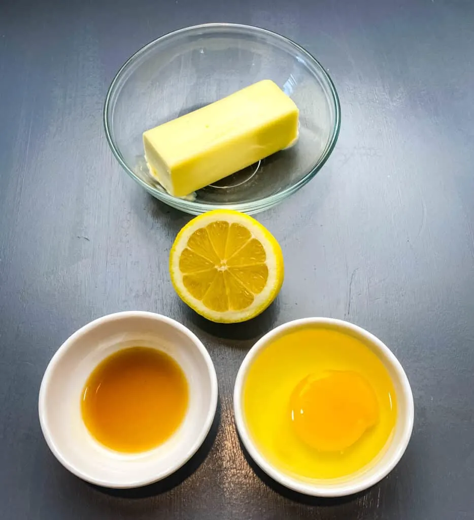 butter, lemon, vanilla, and an egg in glass bowls on a flat surface