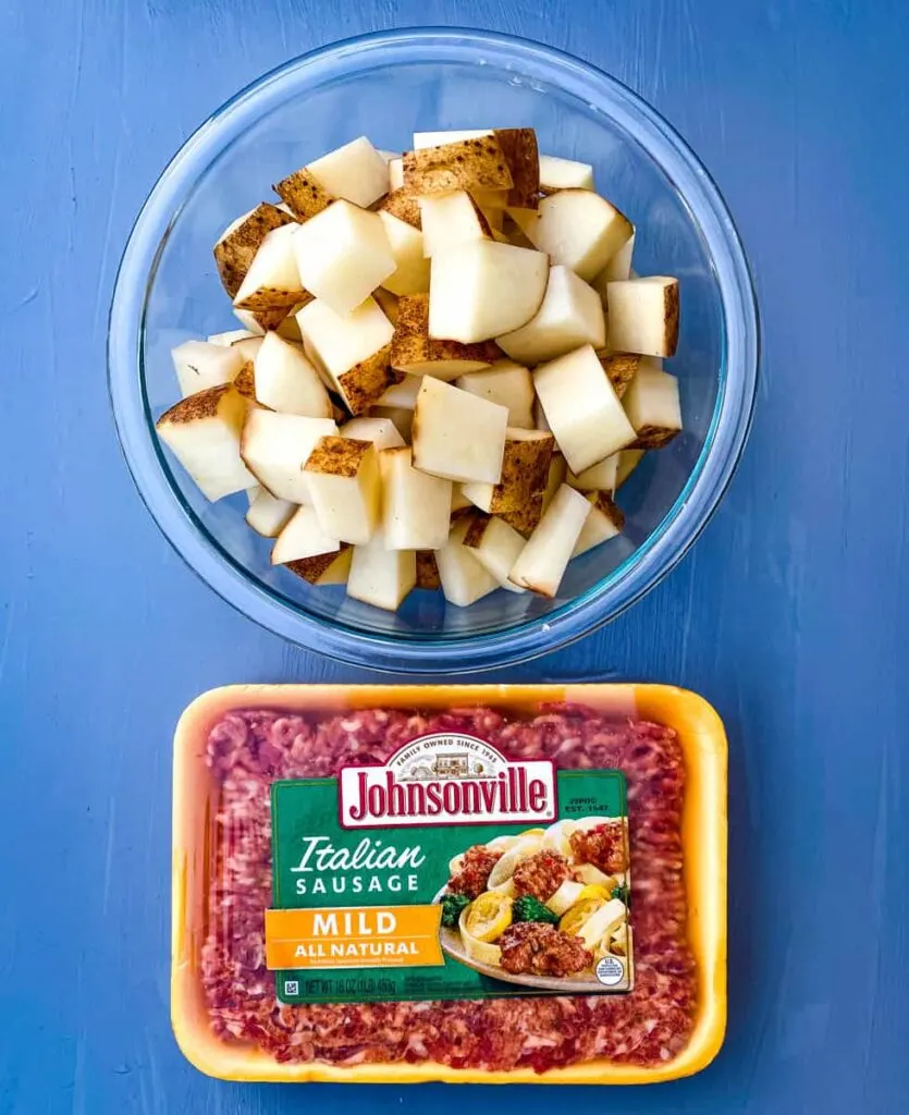 chopped russet potatoes in a glass bowl with a package of Italian sausage