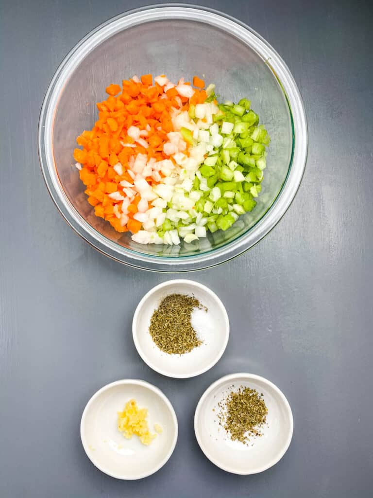 chopped onions, carrots, and celery in a glass bowl along with minced garlic and Italian seasoning