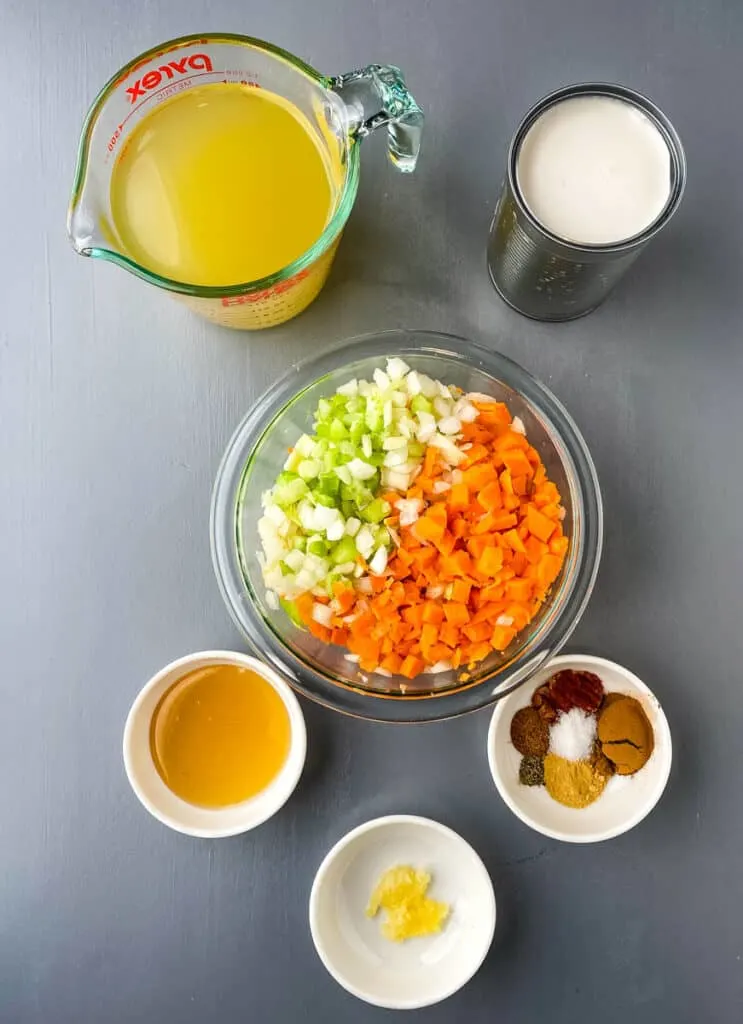 broth, coconut milk, carrots, celery, onions, cinnamon, honey, and garlic in separate bowls on a flat surface