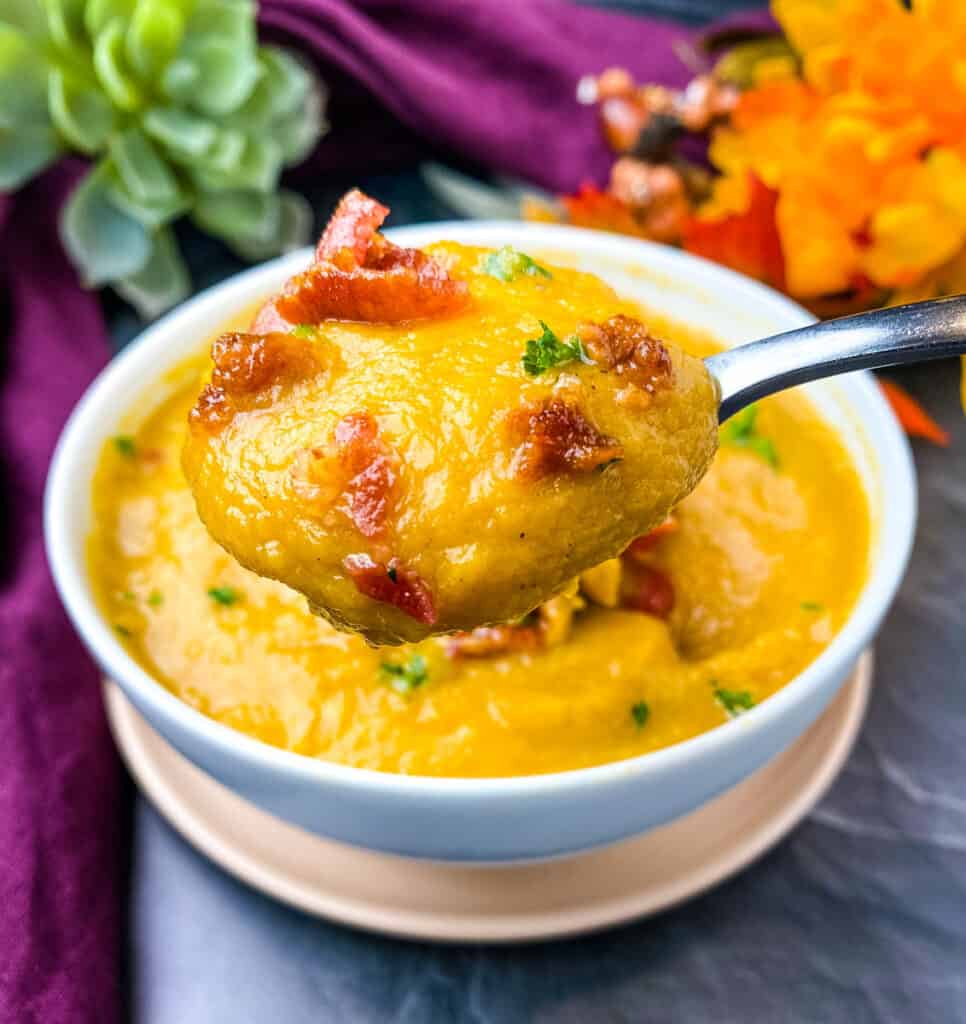 a spoonful of sweet potato soup in a white bowl with chunks of bacon