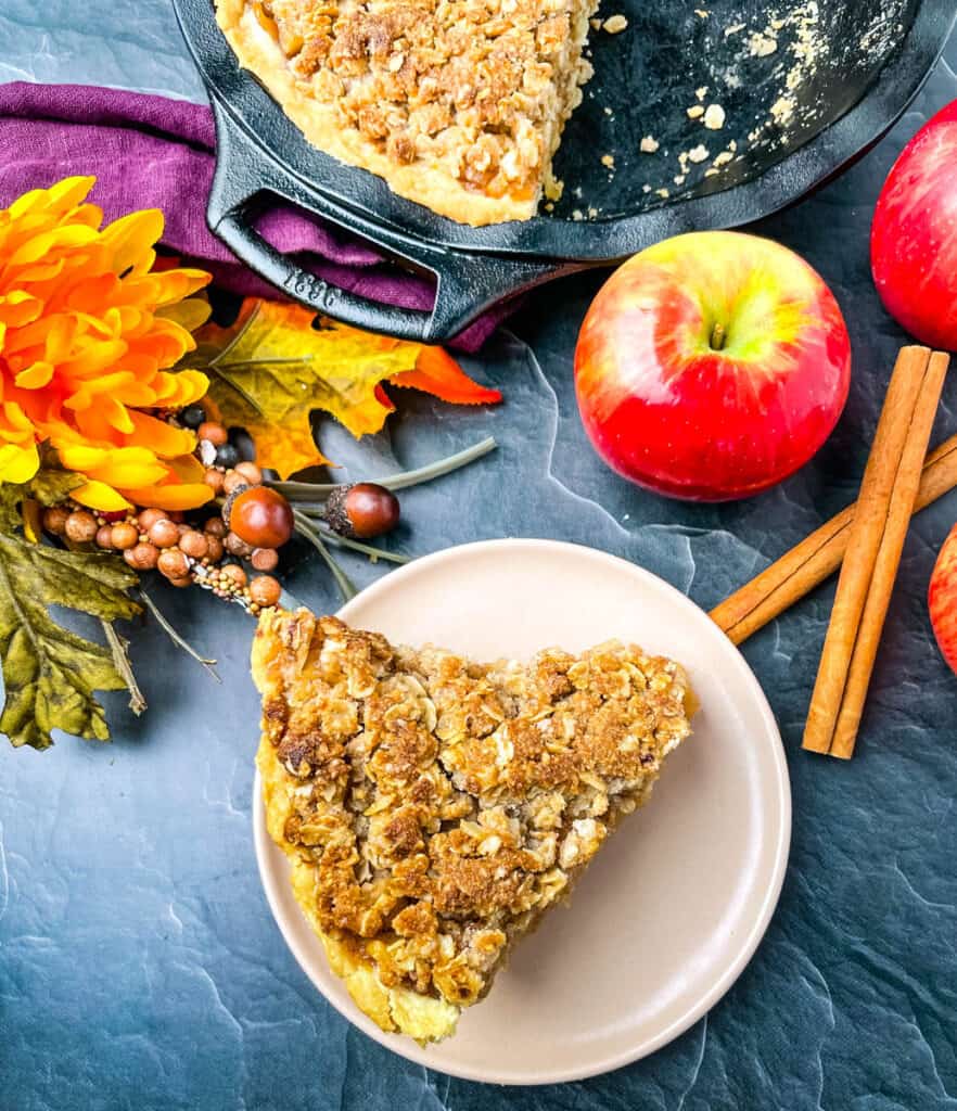 a slice of apple pie on a pink plate with fresh apples