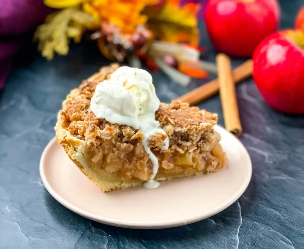 a slice of apple pie on a pink plate with a scoop of ice cream and fresh apples