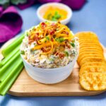 million dollar dip in a white bowl garnished with crackers and celery