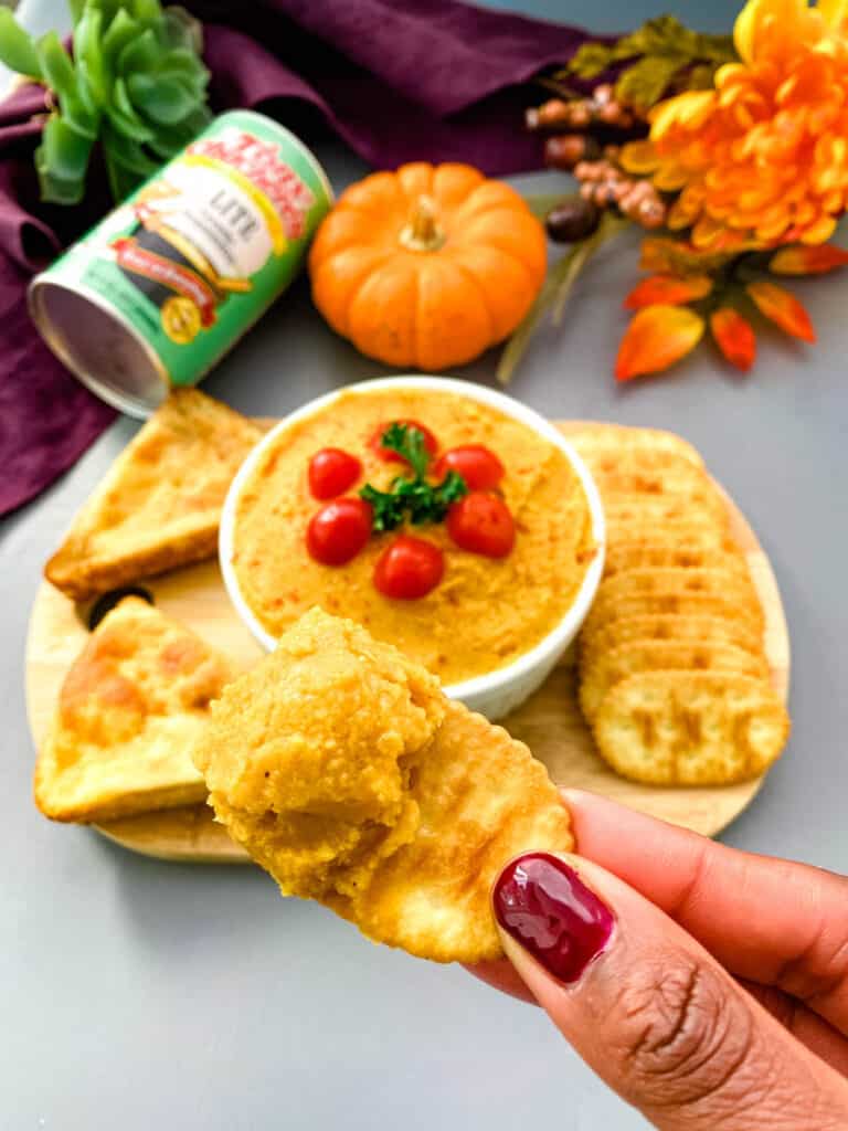 person holding a cracker with pumpkin hummus