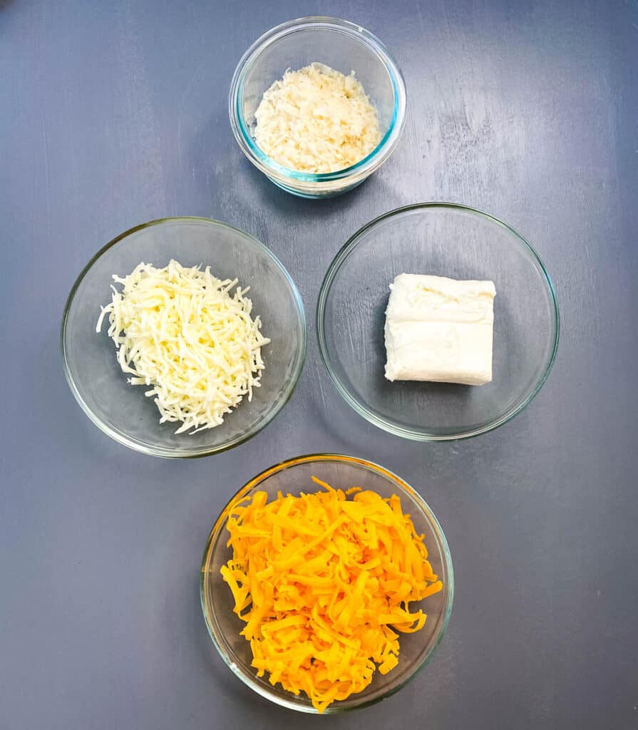 shredded cheddar, shredded mozzarella, cream cheese, and parmesan cheese in separate bowls