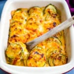 wooden spoon of zucchini au gratin scalloped potatoes in a red baking dish