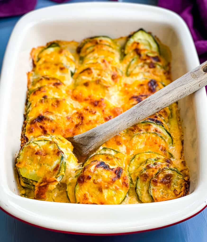 wooden spoon of zucchini au gratin scalloped potatoes in a red baking dish