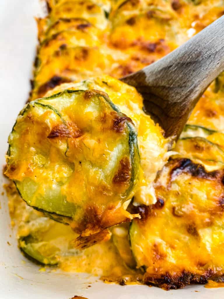 wooden spoon of zucchini au gratin scalloped potatoes in a red baking dish