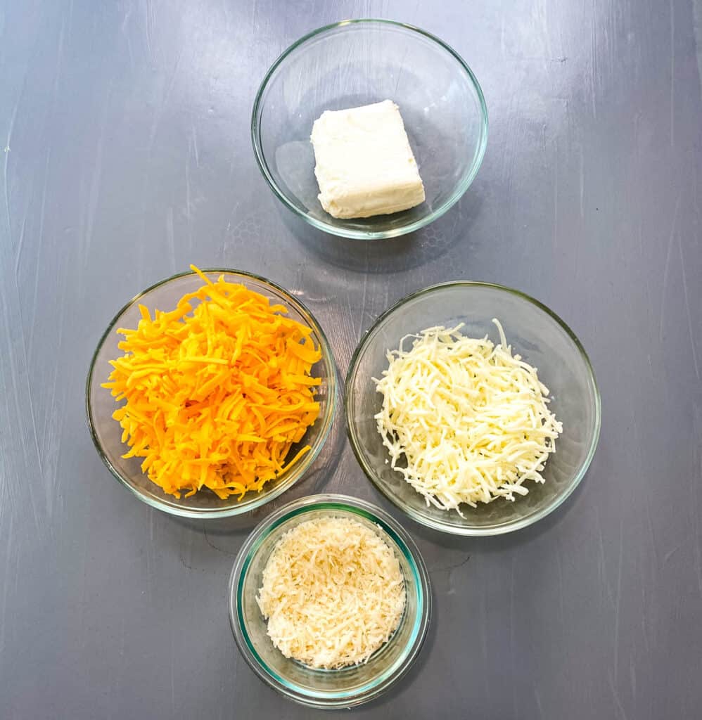 cream cheese, shredded cheddar, mozzarella, and parmesan cheese in separate glass bowls