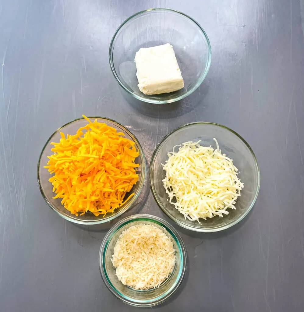 cream cheese, shredded cheddar, mozzarella, and parmesan cheese in separate glass bowls