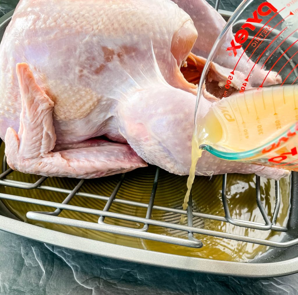 raw turkey in a roasting pan with chicken broth poured into the pan