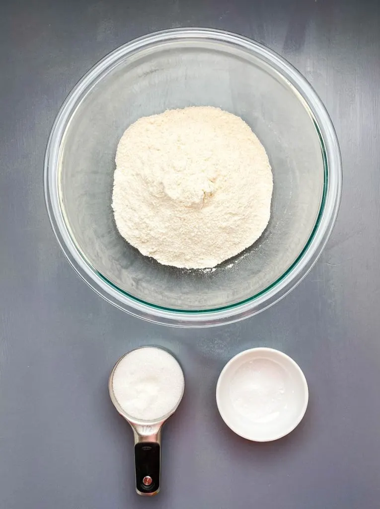 self rising cornmeal, sweetener, and salt in separate bowls on a flat surface