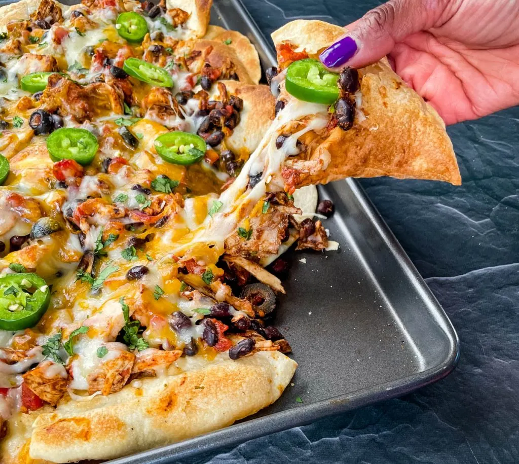 person holding a chip with turkey nachos on a sheet pan