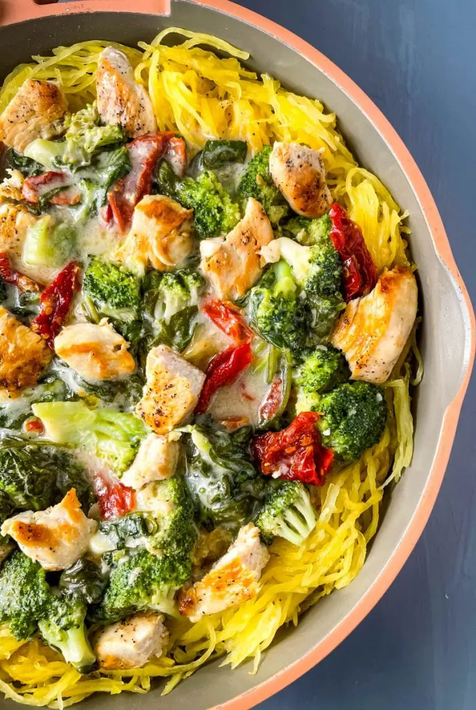 Spaghetti squash chicken alfredo in a pan with broccoli, spinach, and sundried tomatoes