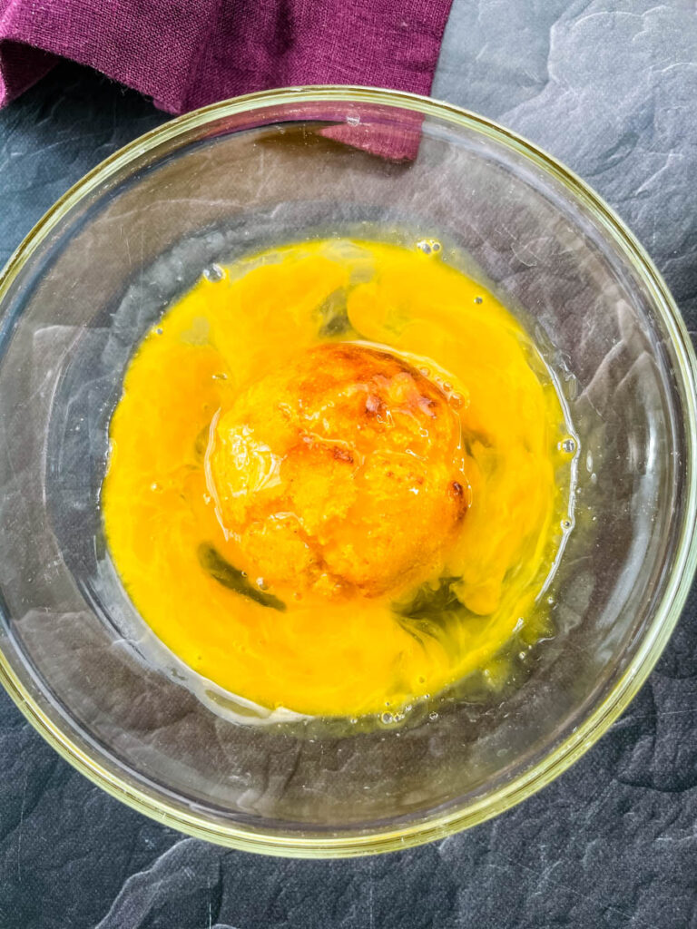 a hushpuppy dredged in raw egg in a glass bowl